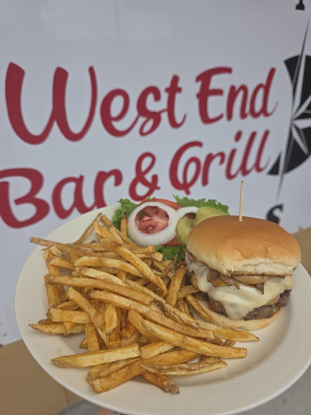 The hand painted West End Bar and Grill sign with the compass rose on the wall, a burger and hand cut fries on a white plate in front of it
